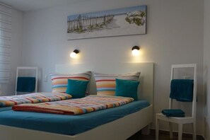 A bedroom with a bed, two bedside tables, a nightstand, a wall-mounted light fixture, and a painting. - Holiday apartment with 2 bedrooms (Norddeich)