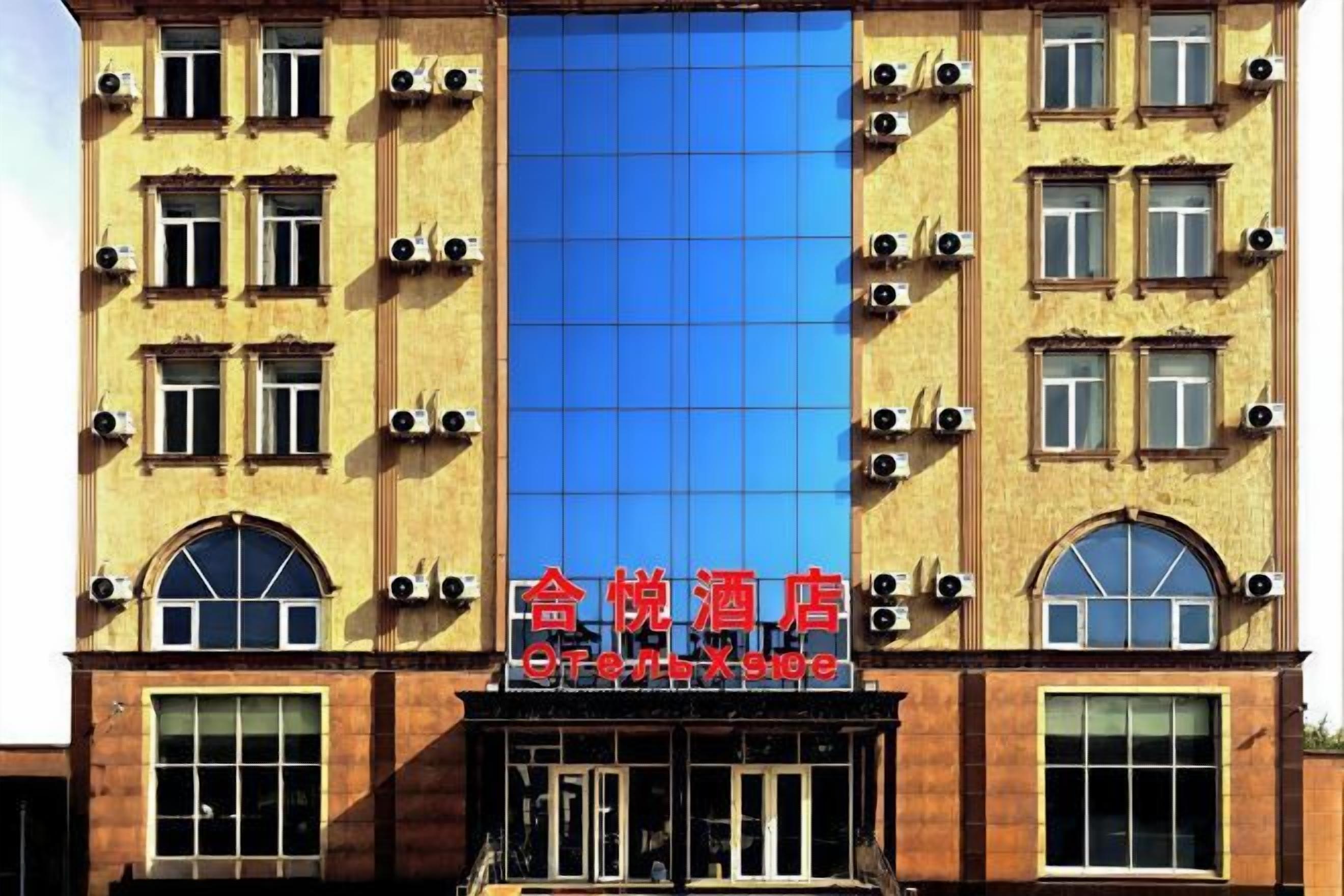 La façade d’un hôtel, avec une grande fenêtre en verre bleu bien visible, plusieurs unités de climatisation et une enseigne avec des caractères chinois.