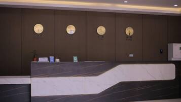 A reception desk with a marble top, clocks on the wall, and a small potted plant.