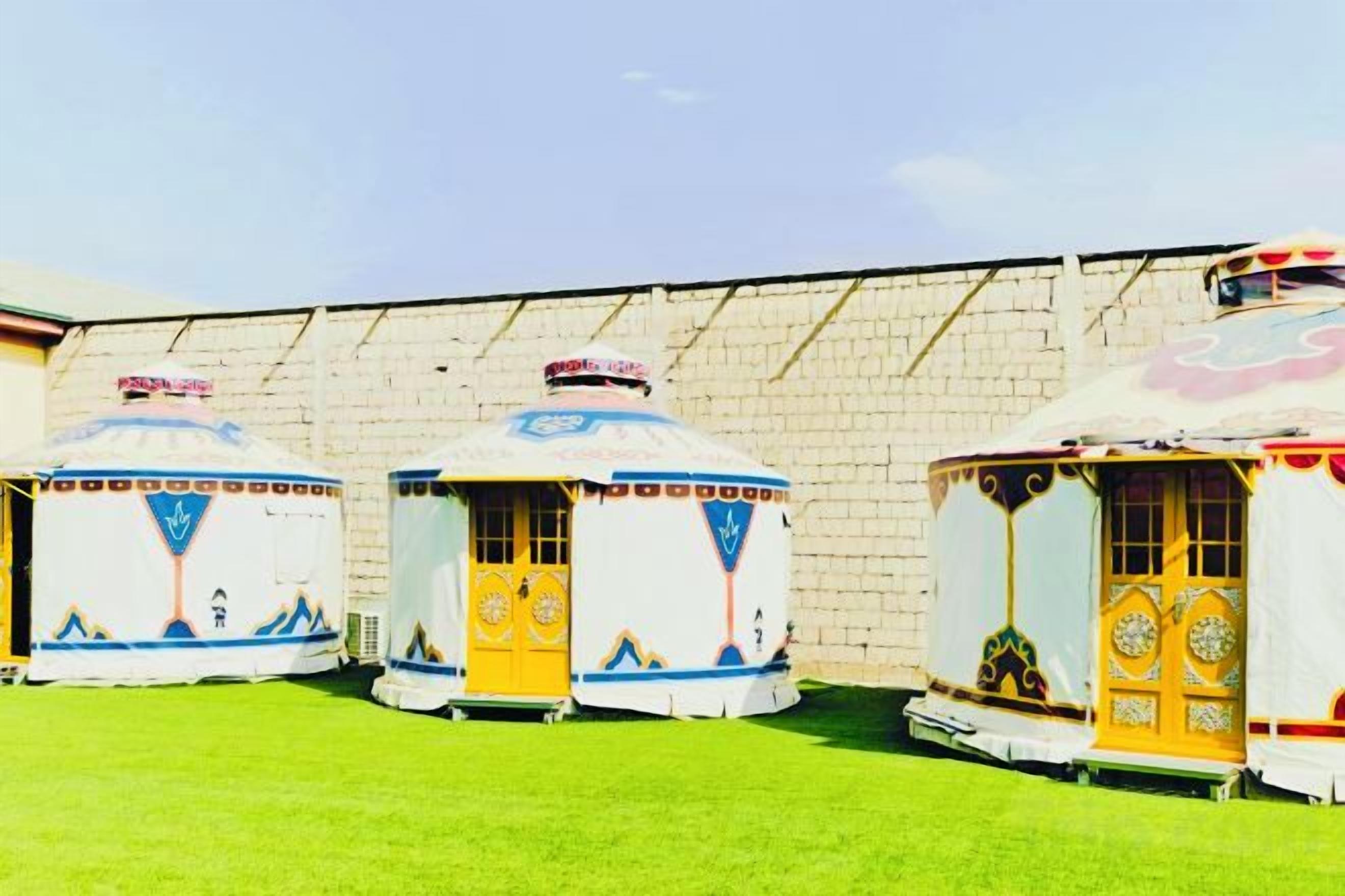 Three yurts with a traditional design, arranged in a row against a brick wall.