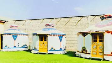 Three yurts with a traditional design, arranged in a row against a brick wall.