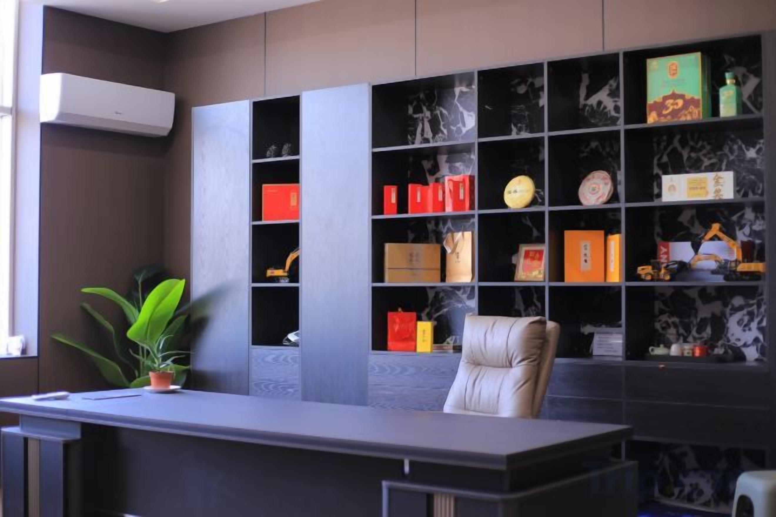 A reception desk with a chair, a potted plant, and a bookshelf with various items.