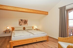 Une chambre à coucher avec un lit en bois, deux tables de chevet avec des lampes, une fenêtre avec des rideaux et un fauteuil en osier.