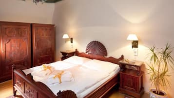 A traditional bedroom with a large bed, two wall-mounted lamps, a potted plant, and a wooden wardrobe.