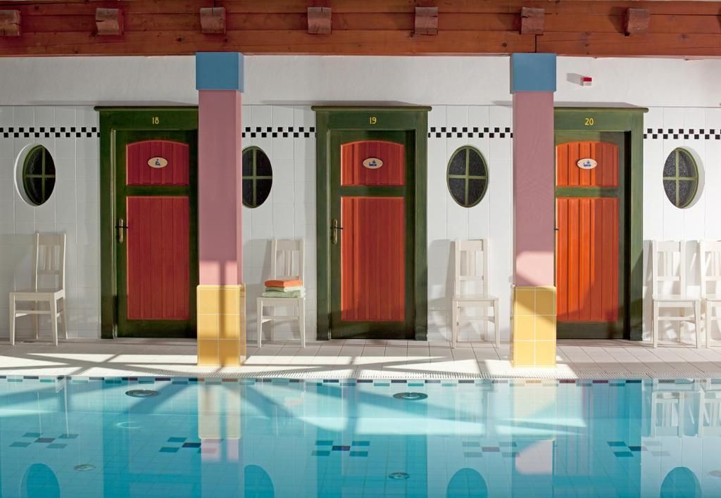 A swimming pool with clear water, surrounded by white chairs and a row of doors numbered 18 to 20.