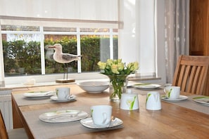 Une table à manger dressée avec de l’assiette blanche, des tasses et un vase rempli de fleurs.