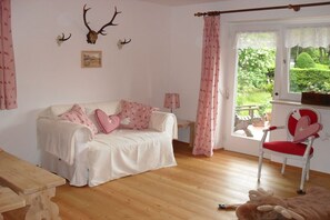A cozy room with a white sofa, a red chair, and a wooden table. - Holiday apartment with 2 bedrooms (Garmisch-Partenkirchen)
