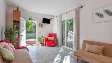 Un amplio salón con una silla roja, un sofá beige y un televisor montado en la pared.