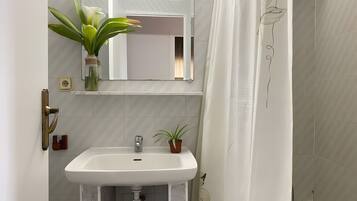 Un baño con un lavamanos blanco, un espejo, una planta en maceta y una cortina de ducha.