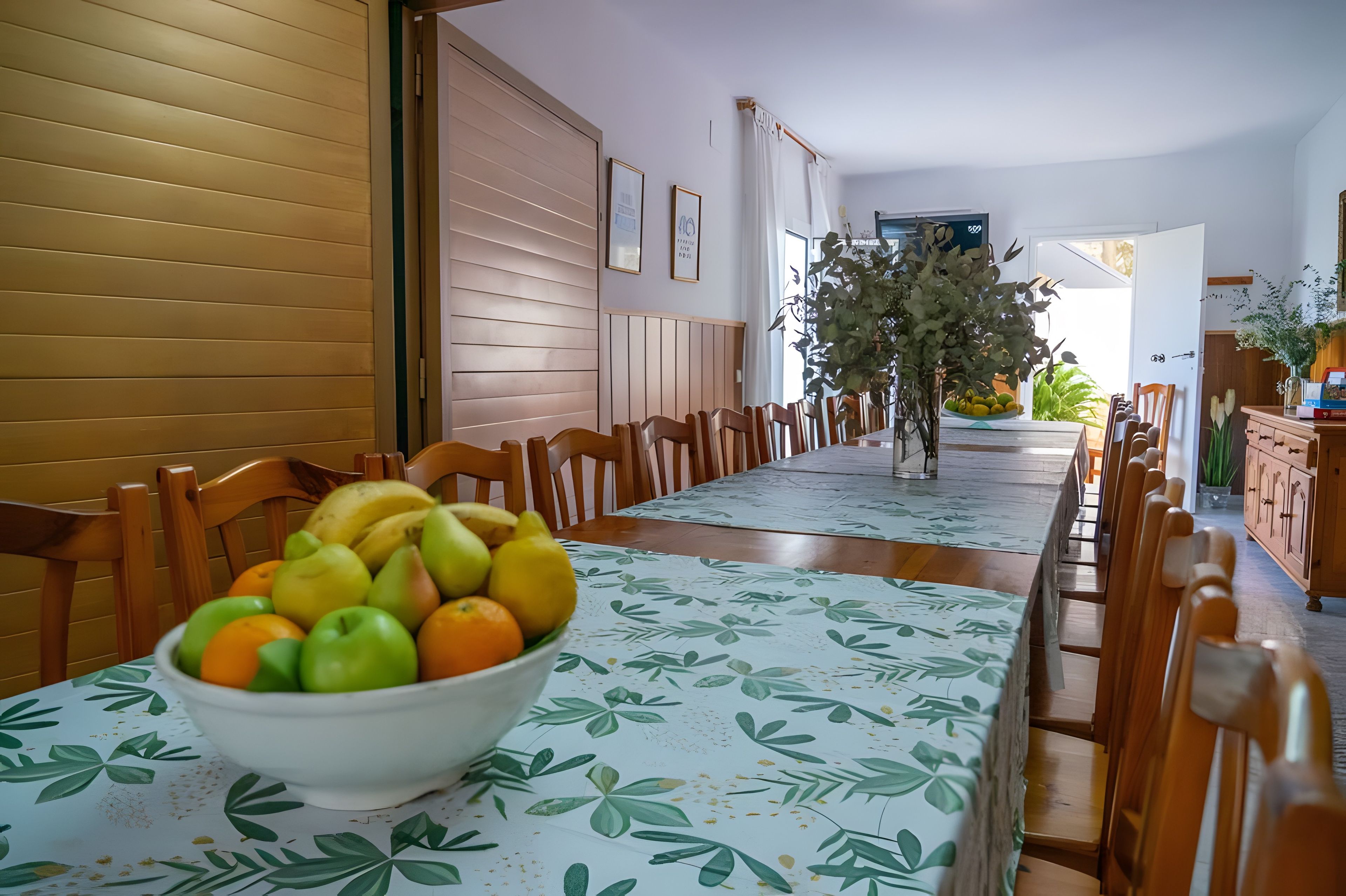 Un comedor con una mesa larga, sillas, un cuenco de fruta y vista a la calle.