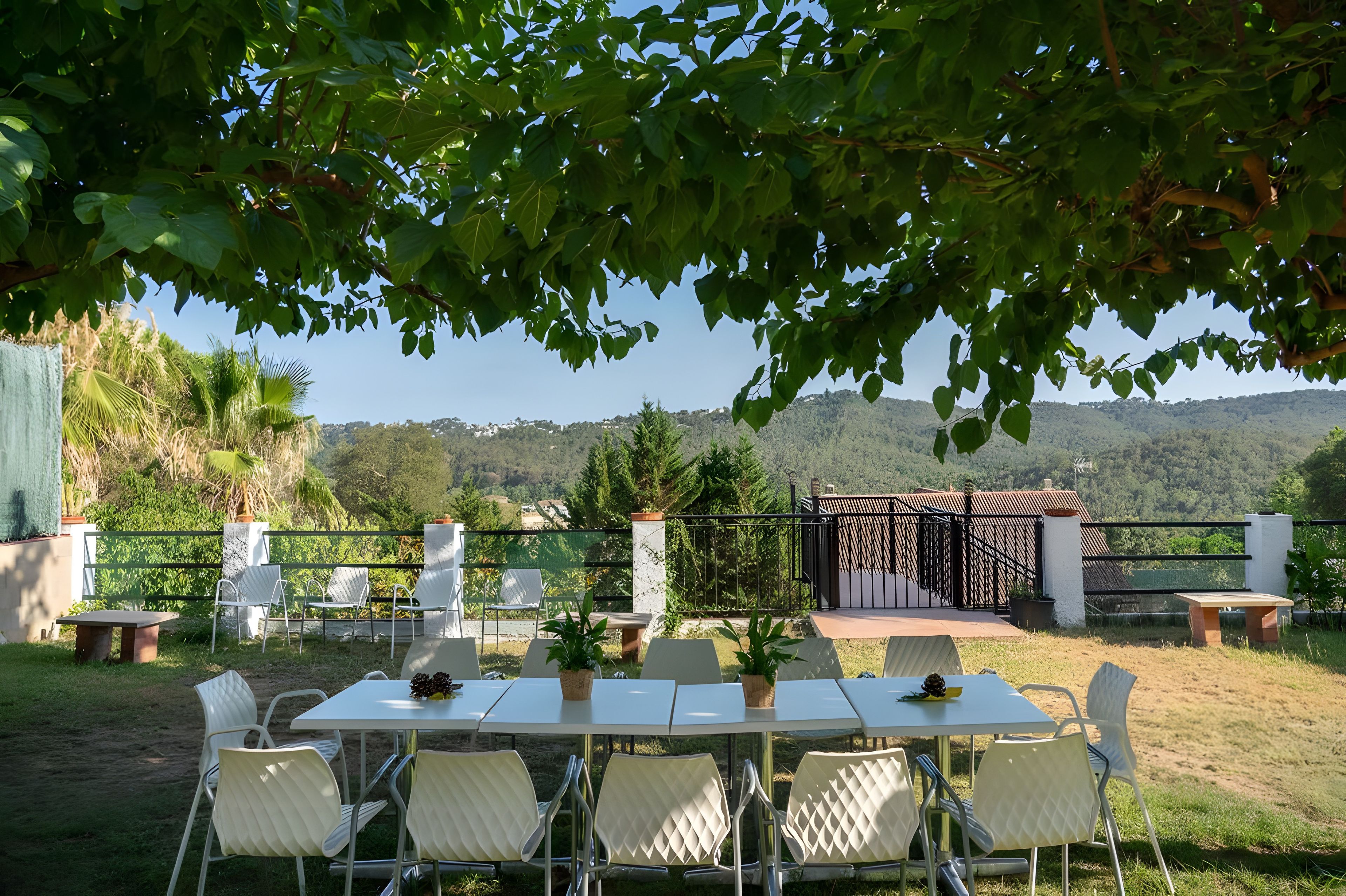 Un espacio de comedor al aire libre con una mesa y sillas, rodeado de follaje y vistas a colinas.
