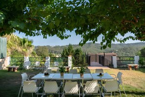 Un espacio de comedor al aire libre con una mesa y sillas, rodeado de follaje y vistas a colinas.