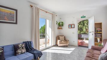 A living room with a blue sofa, a beige armchair, a bookshelf, and a door leading to an outdoor area.