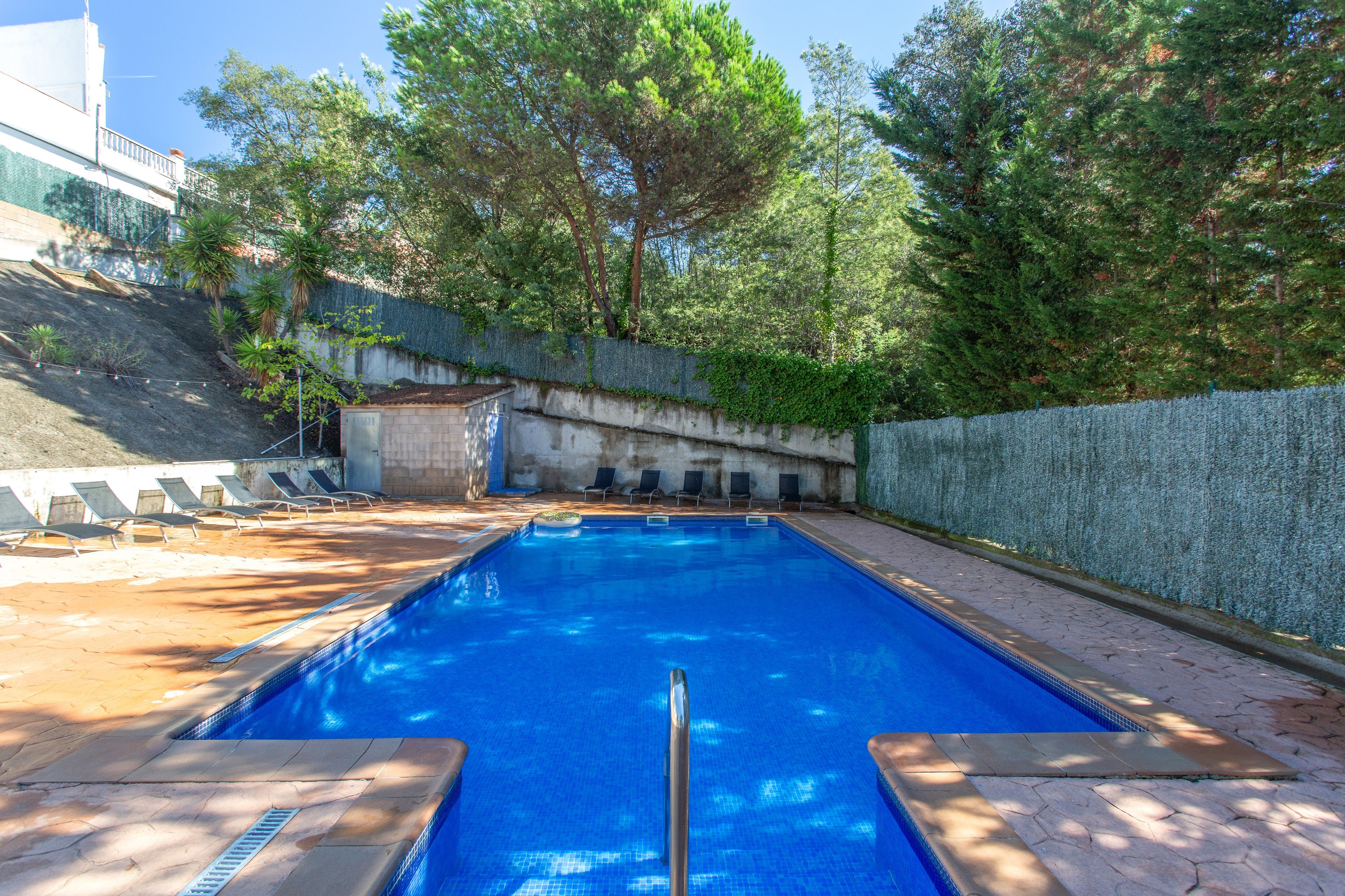 Une piscine à l’eau d’un bleu cristallin, entourée d’une terrasse carrelée et d’un petit muret en pierre.