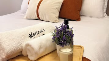 Ein ordentlich bezogenes Bett in Weiß und Braun, ein dekoratives Kissen, ein weißes Handtuch mit Aufschrift, ein kleiner Topfpflanze und eine Kerze auf einem Tablett.