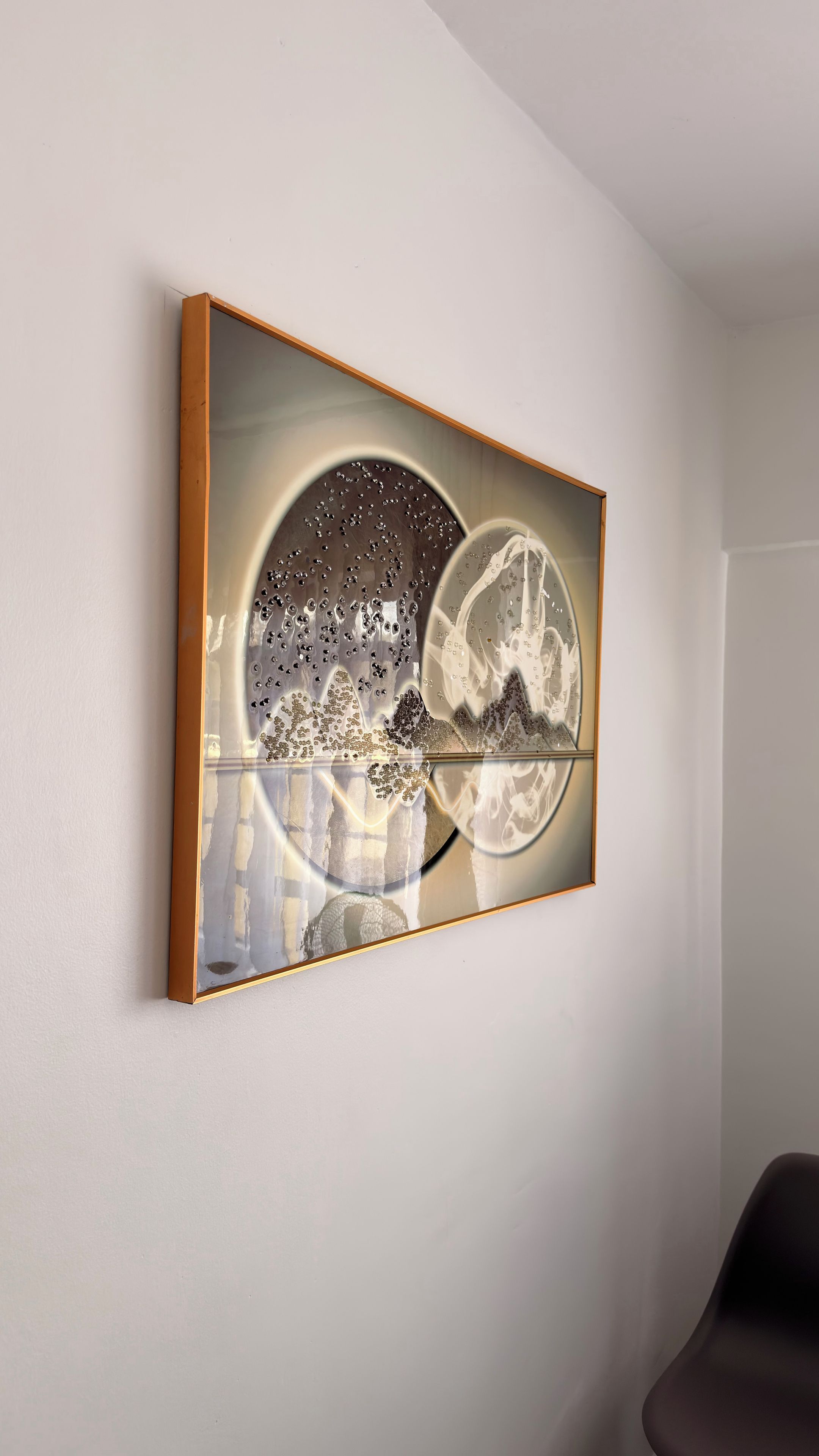 Ein gerahmtes Kunstwerk mit abstrakten Designs und reflektierenden Oberflächen an einer Wand.