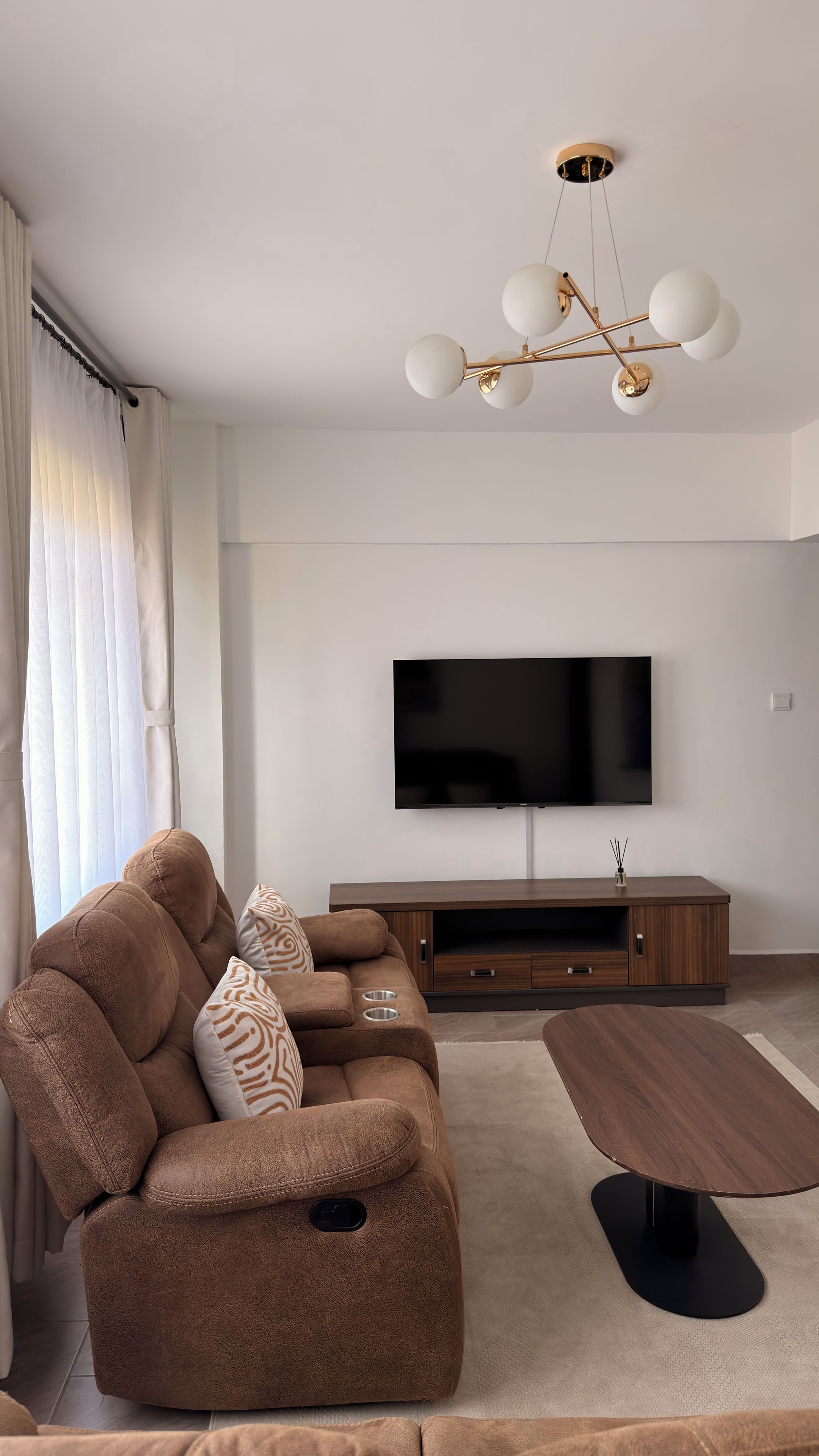 Ein modernes Wohnzimmer mit einem braunen Sofa, einem Flachbildfernseher und einem Holztisch.