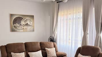 A modern living room with a sectional sofa, a coffee table, a wall-mounted artwork, and a ceiling light fixture.