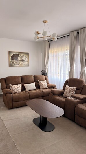 Ein modernes Wohnzimmer mit einer Eckcouch, einem Couchtisch, einem an der Wand befestigten Kunstwerk und einer Deckenleuchte.