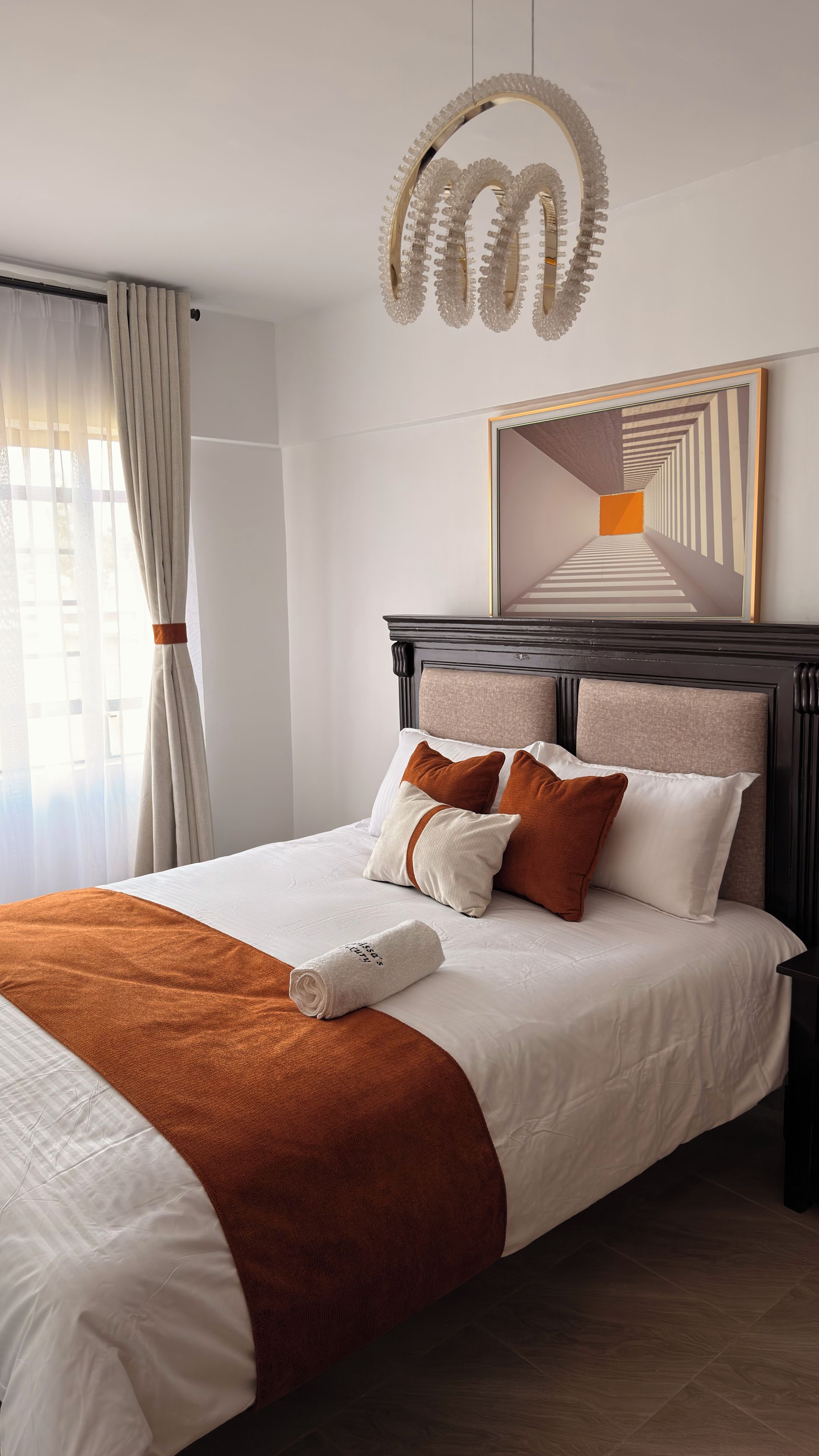 Een hotelkamer met een net opgemaakt bed, een grote spiegel en een moderne kroonluchter.