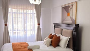 Ein Hotelzimmer mit einem Bett, einem Nachttisch und einem großen Fenster mit Vorhängen.