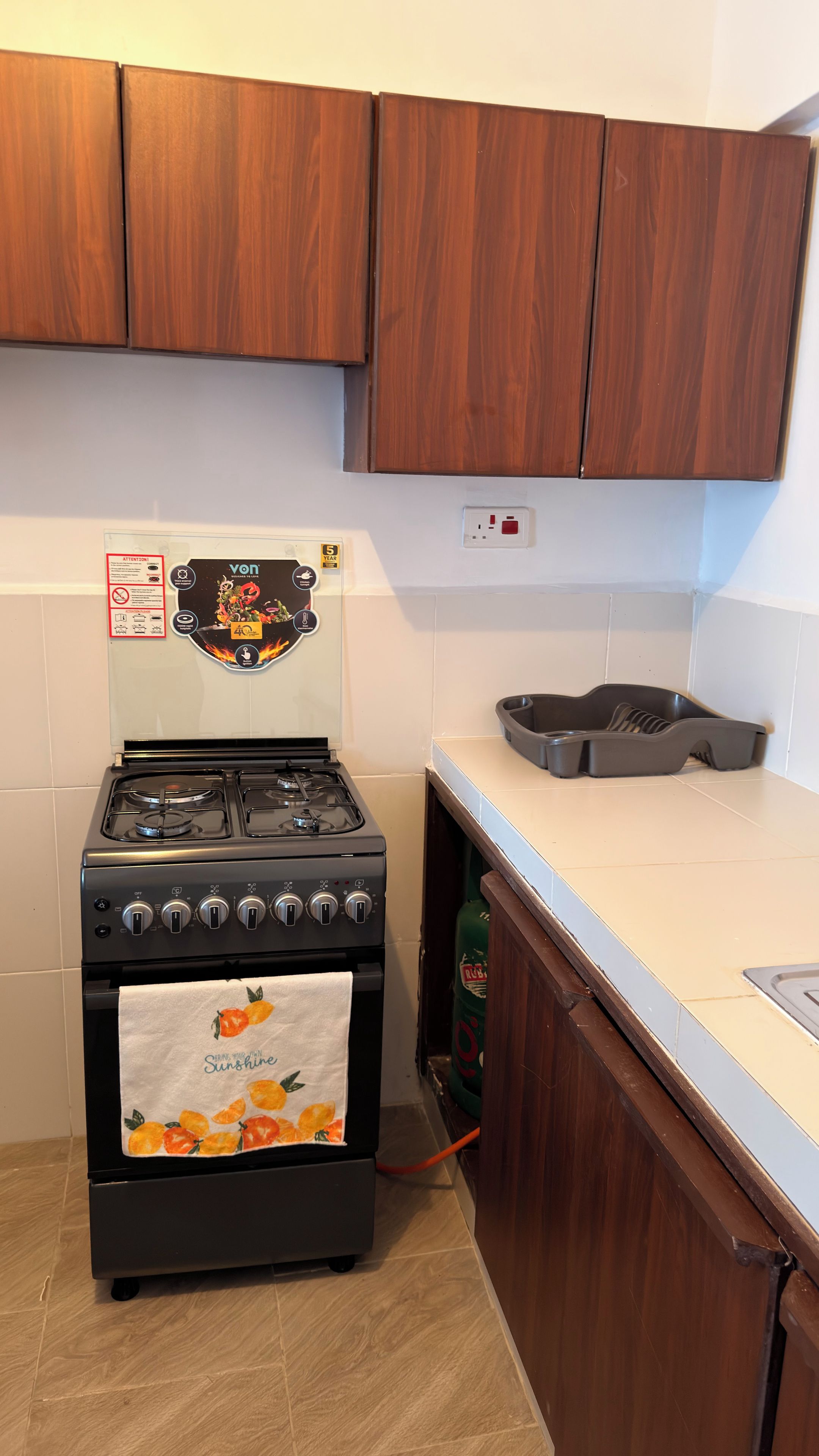Een keuken met een gasfornuis, houten kastjes, een wit aanrechtblad en een wandcontactdoos.