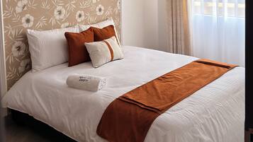 A hotel room with a large bed, a chandelier, floral wallpaper, and a window with curtains.