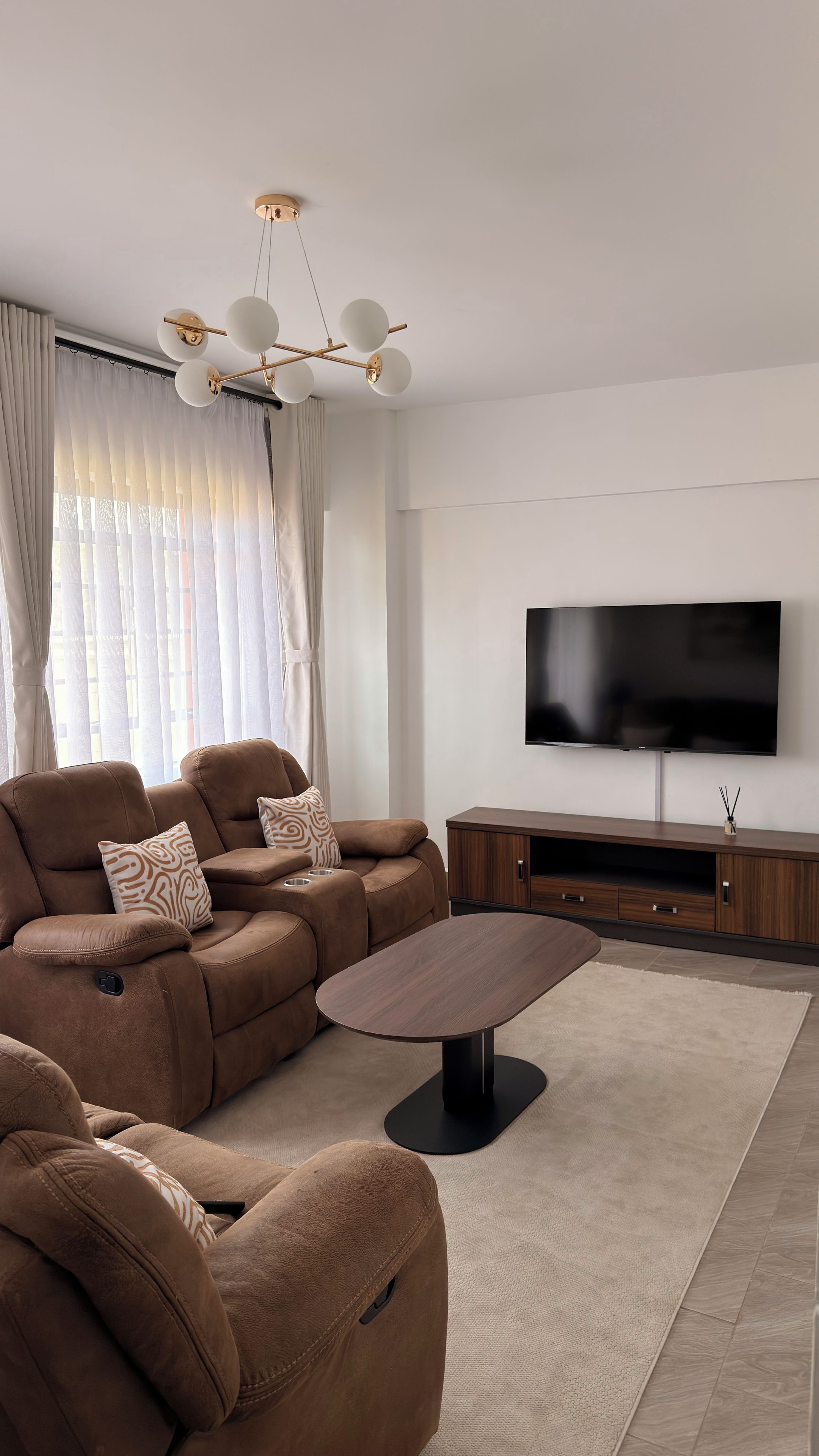 A modern living room with a sectional sofa, a coffee table, a flat-screen TV, and a ceiling light fixture.
