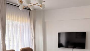A modern living room with a sectional sofa, a coffee table, a flat-screen TV, and a ceiling light fixture.