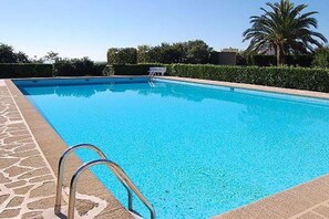 Ein rechteckiger Swimmingpool mit klarer, blauer Wasseroberfläche, umgeben von einer Steinbordsteinkante und einer Metallleiter.