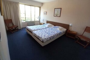 Ein Hotelzimmer mit zwei Betten, einem Vorhangfenster, einem Sessel, einem Nachttisch und einem an der Wand hängenden Bild.