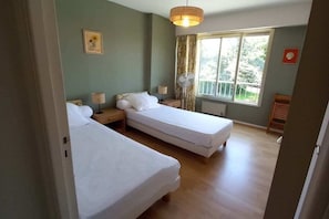 Une chambre avec deux lits, une fenêtre donnant sur un beau paysage, un ventilateur et une lampe.