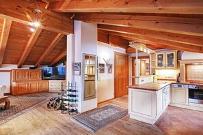 A spacious loft with a high ceiling, wooden beams, a kitchen with white cabinets, and a dining area with a wooden table. - Chalet Tiroler Straße (Reit im Winkl)