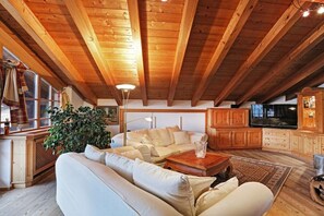 A cozy loft-style living room with a high wooden ceiling, a large sofa, a coffee table, and a television. - Chalet Tiroler Straße (Reit im Winkl)