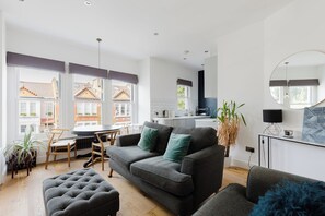 Ein modernes Wohnzimmer mit einem grauen Sofa, einem runden Esstisch und einer Küchenzeile im Hintergrund.