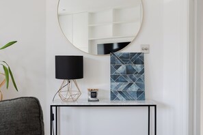 Ein Zimmer mit einem runden Spiegel, einer schwarzen Lampe, einer blau gemusterten Fliese und einem kleinen Tisch mit einer Kerze.