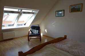 A room with a sloped ceiling, a bed, a chair, and two windows. - Holiday home with 4 bedrooms (Wangerooge)