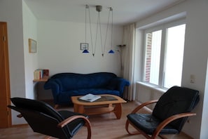 A living room with a blue sofa, two black leather chairs, a wooden coffee table, and a window with curtains. - Holiday home with 4 bedrooms (Wangerooge)