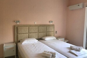 Una cama doble con sábanas y almohadas blancas, dos mesitas de noche y un aire acondicionado instalado en la pared.