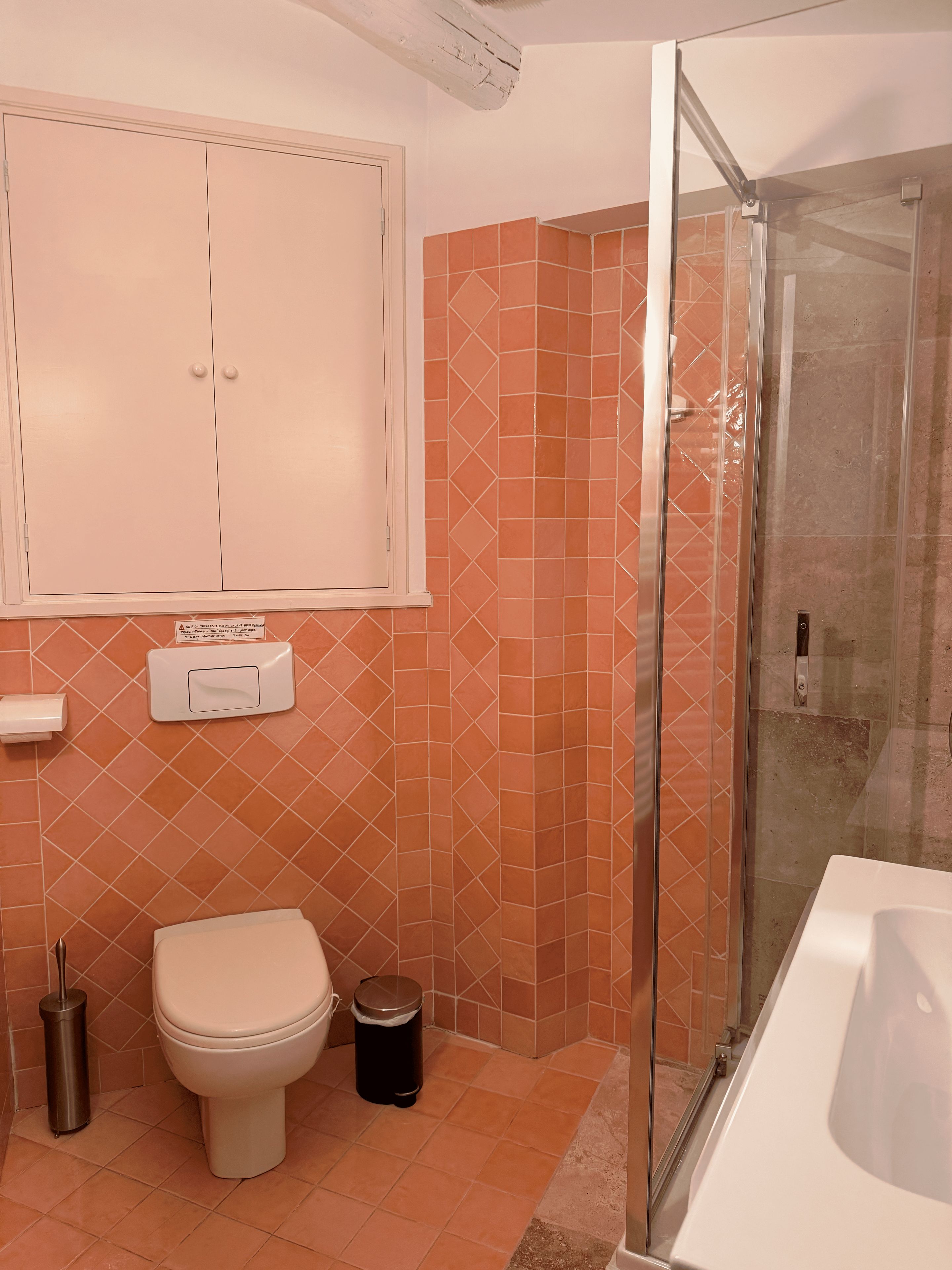 Une salle de bain comprenant des toilettes, un bidet, une poubelle et une douche séparée par une paroi en verre.