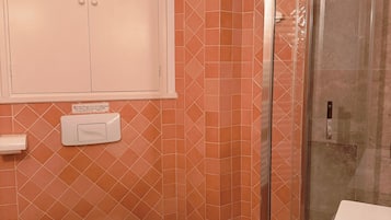 Une salle de bain comprenant des toilettes, un bidet, une poubelle et une douche séparée par une paroi en verre.