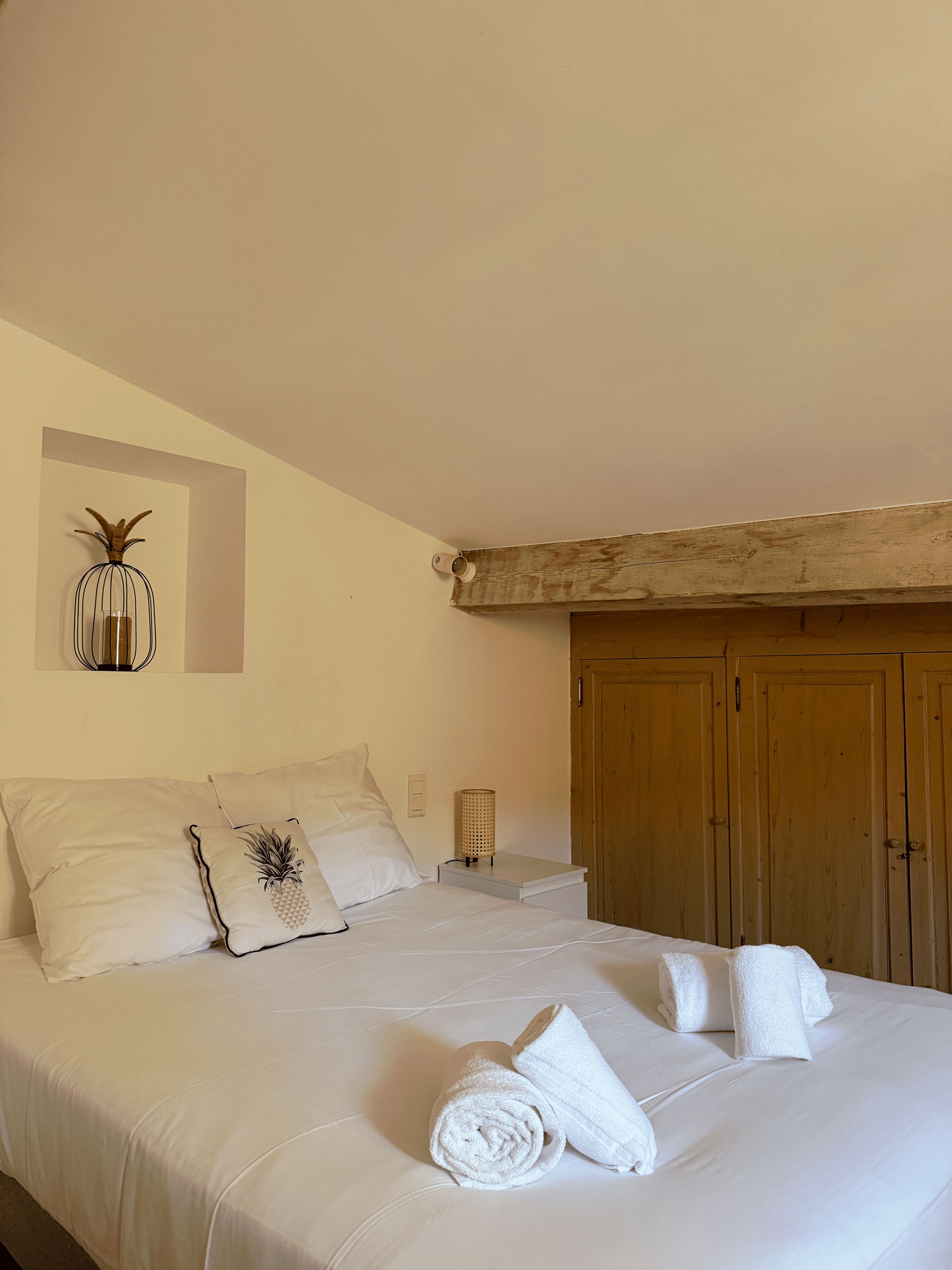 Une chambre à coucher avec un lit, des oreillers, une table de chevet, une lampe et une armoire.
