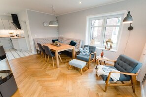 Ein modernes Wohnzimmer mit Holzdielen im Fischgrätmuster, einem Esstisch mit Stühlen, einer Couch und einem Fenster mit Blick.