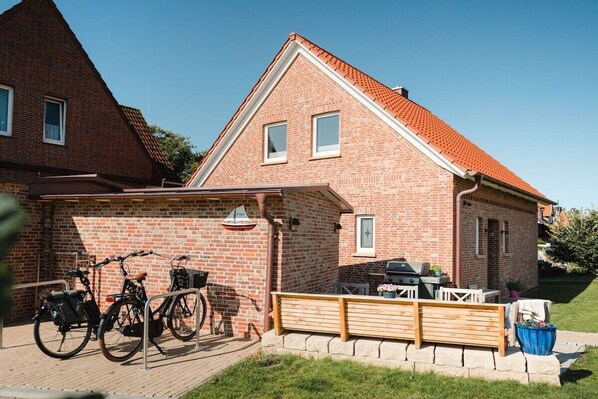 Ein Backsteinhaus mit einer überdachten Terrasse, einem Fahrrad und einem Grill.