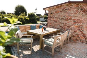 Eine Terrasse im Freien mit einem Holztisch und Stühlen, einer Ziegelwand und einem Blumentopf.