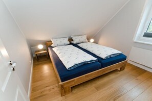 Ein kleines Zimmer mit einem Einzelbett, schrägen Wänden, Holzboden und einem Fenster für natürliches Licht.