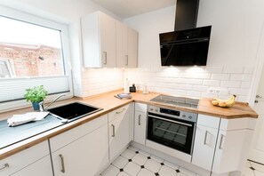 Een moderne keuken met witte kastjes, een zwarte afzuigkap, een ingebouwde oven en een raam met uitzicht op een gebouw van baksteen.