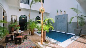 A pool area with a tiled floor, palm trees, and a table with chairs. - Riad Dabachi (Marrakech)