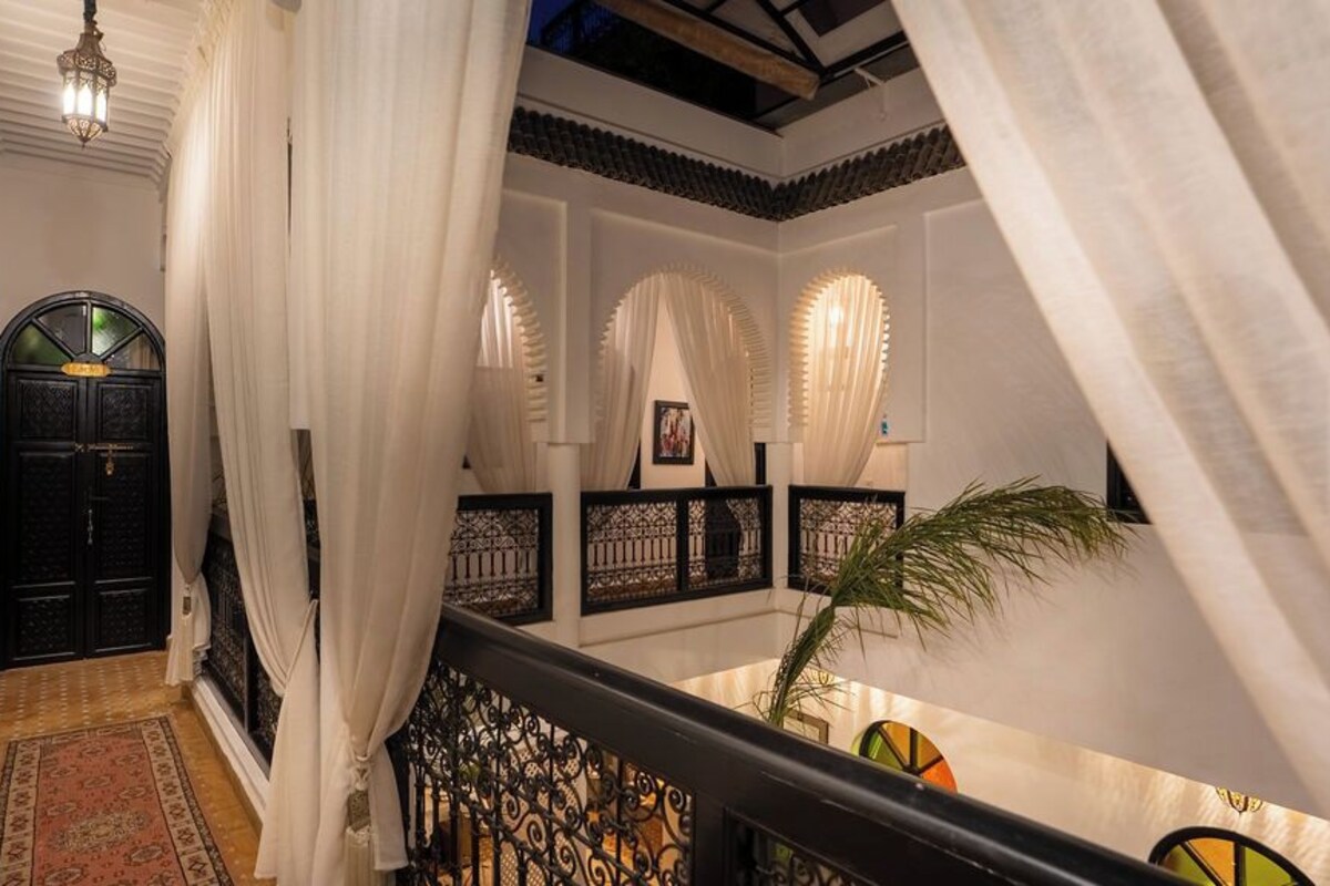 A corridor with a black door, white curtains, and a staircase with black railings.