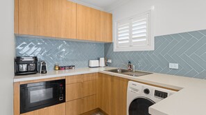 A compact kitchen with a microwave, toaster, sink, and washing machine. - Seascape Studio in Terrigal (Terrigal)